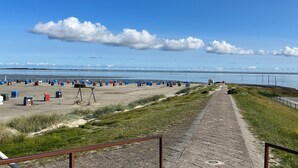 A beach with portable toilets and a paved walkway leading to the water. - Ferienwohnung im Erdgeschoss in Nessmersiel (Dornum)