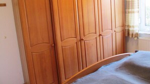 A bedroom with a wooden wardrobe, a bed with a blue blanket, and a window with curtains. - Ferienwohnung im Erdgeschoss in Nessmersiel (Dornum)