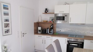 A compact kitchen with white cabinets, a microwave, a coffee maker, and an oven. - Ferienwohnung im Erdgeschoss in Nessmersiel (Dornum)