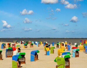 Strandhütten mit Nummern, in Reih und Glied auf sandigem Strand angeordnet, mit Blick auf das Meer und den Horizont.