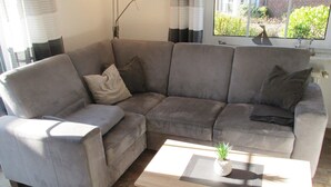 A sectional sofa with a small table and a plant. - Ferienwohnung im Erdgeschoss in Nessmersiel (Dornum)