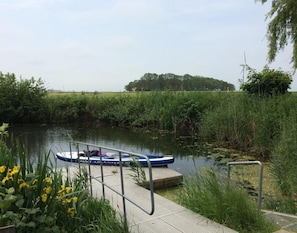 A calm river with a dock and a boat. - Ferienwohnung im Erdgeschoss in Nessmersiel (Dornum)