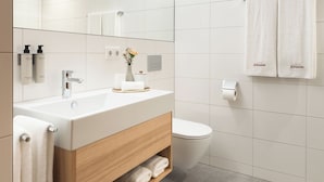 A modern bathroom with a white sink, wooden vanity, and a toilet. - Hotel Johann (Lauterach)