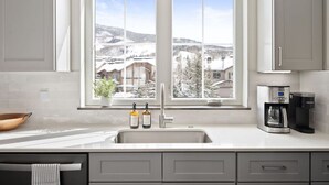 A kitchen with a large window, a sink, a coffee maker, and two bottles on the counter. - Modern Mountain Retreat (Silverthorne)