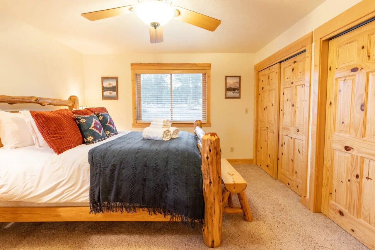 A bedroom with a wooden bed, a ceiling fan, a window with blinds, and wooden closets.