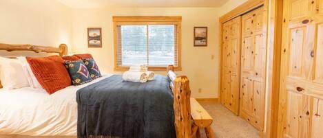 A bedroom with a wooden bed, a ceiling fan, a window with blinds, and wooden closets.
