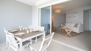 Een moderne eethoek met een witte tafel gedekt voor vier personen, een bank en een vloerlamp in de aangrenzende woonkamer.