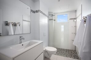A modern bathroom with a white sink, mirror, and toilet. There is a glass shower enclosure with a checkered floor. - Horizon Bleu "feet in the water (Les Trois Ilets)
