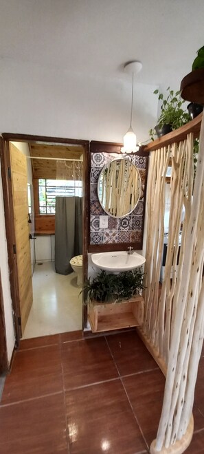 Un baño con suelo de madera, un lavabo, un espejo y una lámpara en el techo.