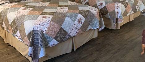 Una habitación de hotel con dos camas, cada una cubierta con un edredón de retazos. Hay un cuadro enmarcado en la pared sobre las camas, una lámpara de noche y una mesita entre las camas.