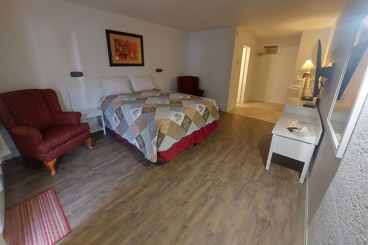 A bedroom with a bed, a red armchair, a bedside table, and a dresser.