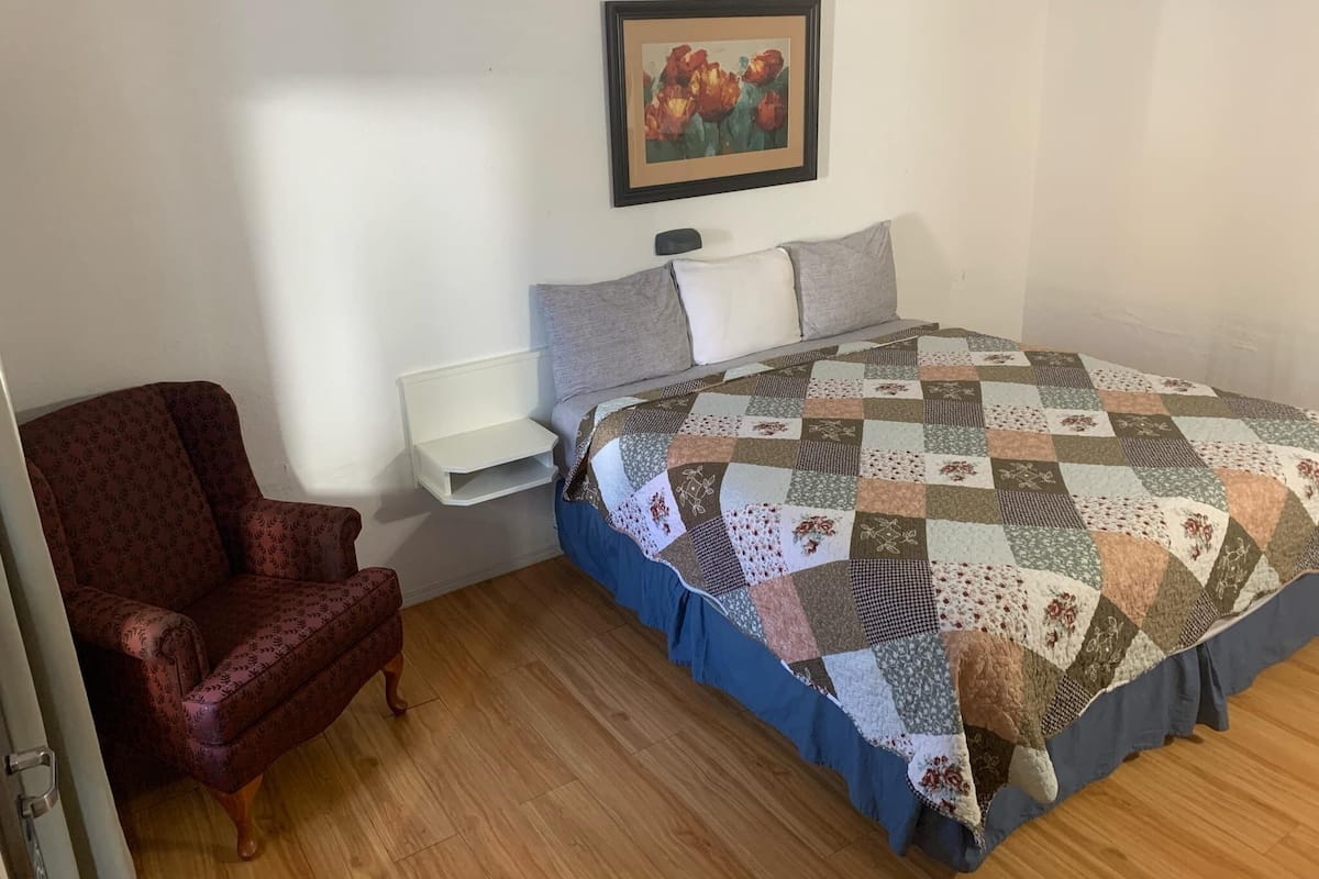 A bedroom with a bed, a chair, a bedside table, and a painting on the wall.
