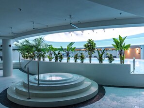 Un área de piscina interior moderna con escalones escalonados que bajan al agua, rodeada de plantas en macetas y un techo curvo.