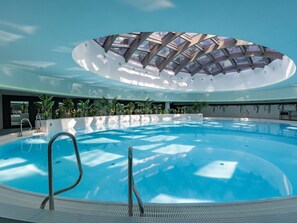 Swim laps in a spacious pool surrounded by lush greenery and natural light pouring in through a stunning skylight.
