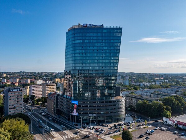Contemporary building with a curved glass facade, surrounded by a parking area and urban greenery.