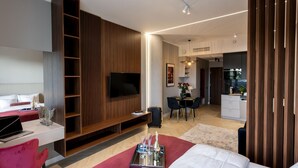 A modern hotel room with a large bed, a desk with a laptop, a TV mounted on a wooden panel, a dining area with a table and chairs, and a kitchen in the background. - Comfortable Apartment, Center of Szczecin (Szczecin)