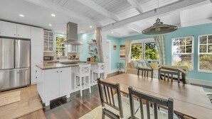 A modern kitchen with white cabinetry, a stainless steel refrigerator, and a dining area with a wooden table and chairs. - Secluded Cottage with Beach Access! [Cove Cottage] (Tremont)