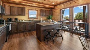 A spacious kitchen with wooden cabinets, a granite countertop, and a large island with stools. - Brand New ~ Smoky Mountain Trailhead ~ Panoramic Views & Indoor Pool (Sevierville)