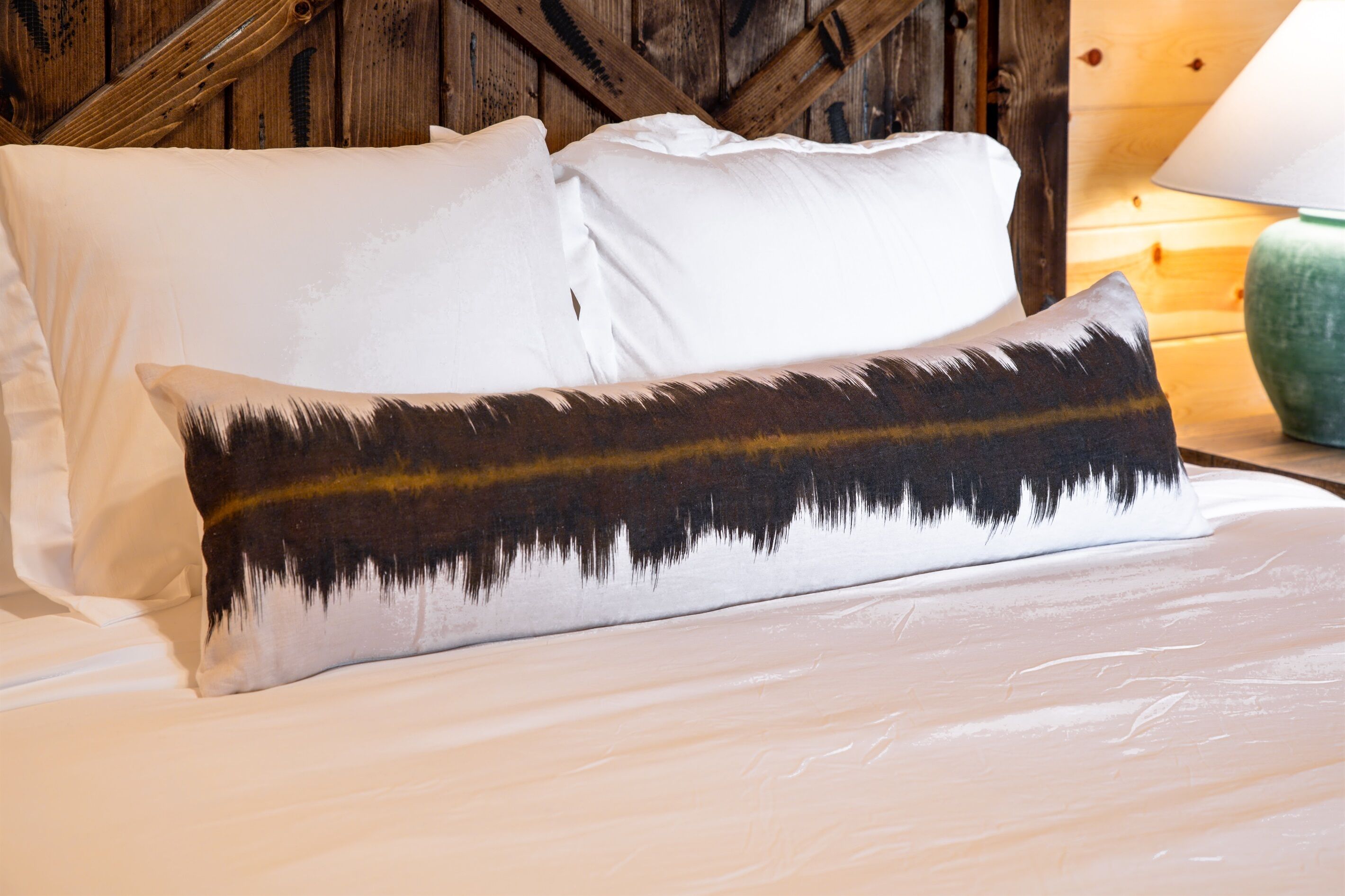 A bed with white bedding and a single decorative pillow with a nature-inspired design.