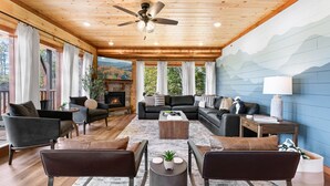 A spacious living room with a fireplace, comfortable seating, and a large window overlooking a scenic view. - Brand New ~ Smoky Mountain Trailhead ~ Panoramic Views & Indoor Pool (Sevierville)