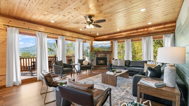 A spacious living room with wooden floors, a fireplace, and large windows offering a mountain view. - Brand New ~ Smoky Mountain Trailhead ~ Panoramic Views & Indoor Pool (Sevierville)