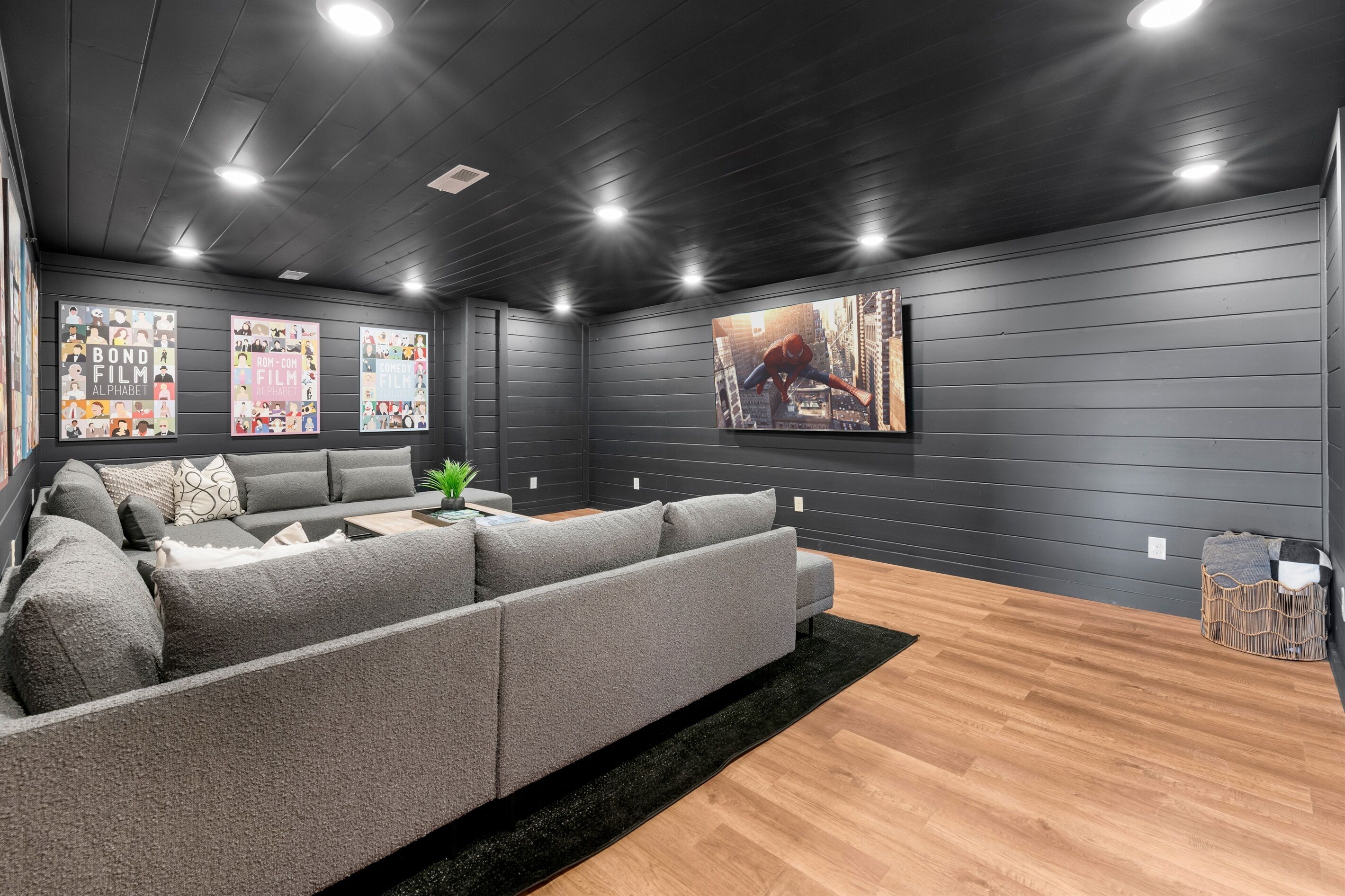 Een moderne woonkamer met een grijze modulaire bank, een zwart vloerkleed en een grote tv aan de muur.