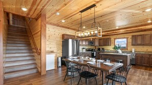 A wooden interior with a staircase, kitchen, dining area, and a view through a window. - Brand New ~ Smoky Mountain Trailhead ~ Panoramic Views & Indoor Pool (Sevierville)