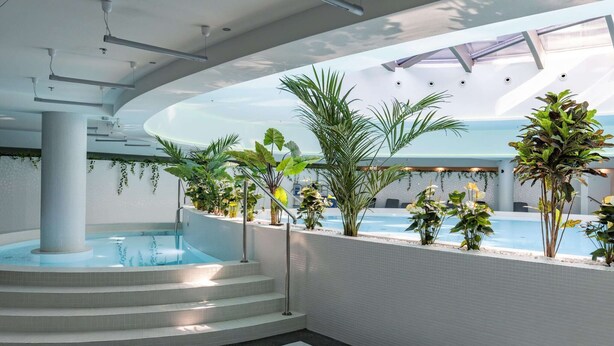 A modern indoor pool area with a central water feature, surrounded by steps and various plants. - Apartment in Szczecin With Pool and Sauna (Szczecin)