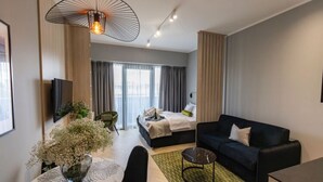 A modern hotel room with a bed, a black sofa, a dining area with a table and chairs, and a large window with curtains. - Apartment in Szczecin With Pool and Sauna (Szczecin)