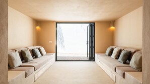 A modern room with a beige sofa set, a glass door leading outside, and two wall-mounted lights. - 3 Bedroom Villa, Private Pool, 500m to Binisafua Beach (Binisafau)