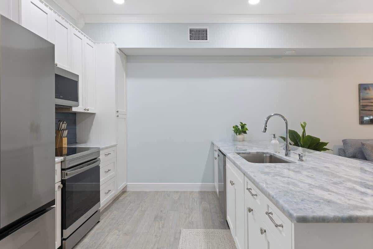 A modern kitchen with white cabinetry, stainless steel appliances, and a marble countertop.