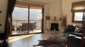 Un salón espacioso con un amplio ventanal corredera que da a un balcón, chimenea, sofá de cuero y candelabro.