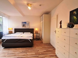 A bedroom with a bed, bedside lamps, a dresser, a painting, and a ceiling light fixture. - Ferienhaus in Bojendorf mit Terrasse (Fehmarn)