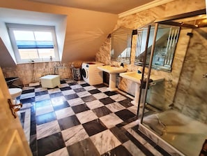 A bathroom with a checkered floor, a washing machine, two sinks, a glass shower enclosure, and a window. - Ferienhaus in Bojendorf mit Terrasse (Fehmarn)