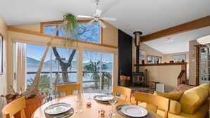 Un coin repas avec une grande table dressée pour quatre personnes, un canapé et une vue sur un lac et des montagnes.