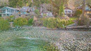 Une zone résidentielle côtière où se trouvent des maisons construites sur un littoral rocheux, entourée d’une forêt dense.