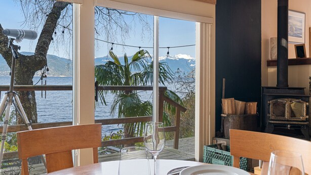 Un coin repas avec une table dressée pour deux personnes, offrant une vue panoramique sur un lac et des montagnes.