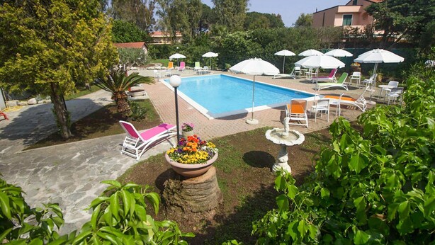 Une piscine entourée de verdure et d’un sentier en pierre, avec des chaises longues et des parasols.