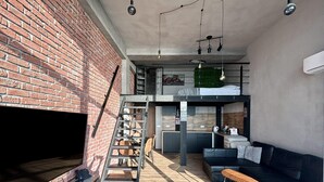 A loft-style living space with a brick wall, a loft bed, a kitchen area, and a seating area with a sofa and a small table. - Apartment in Dziwnowek With Sea View (Dziwnów)
