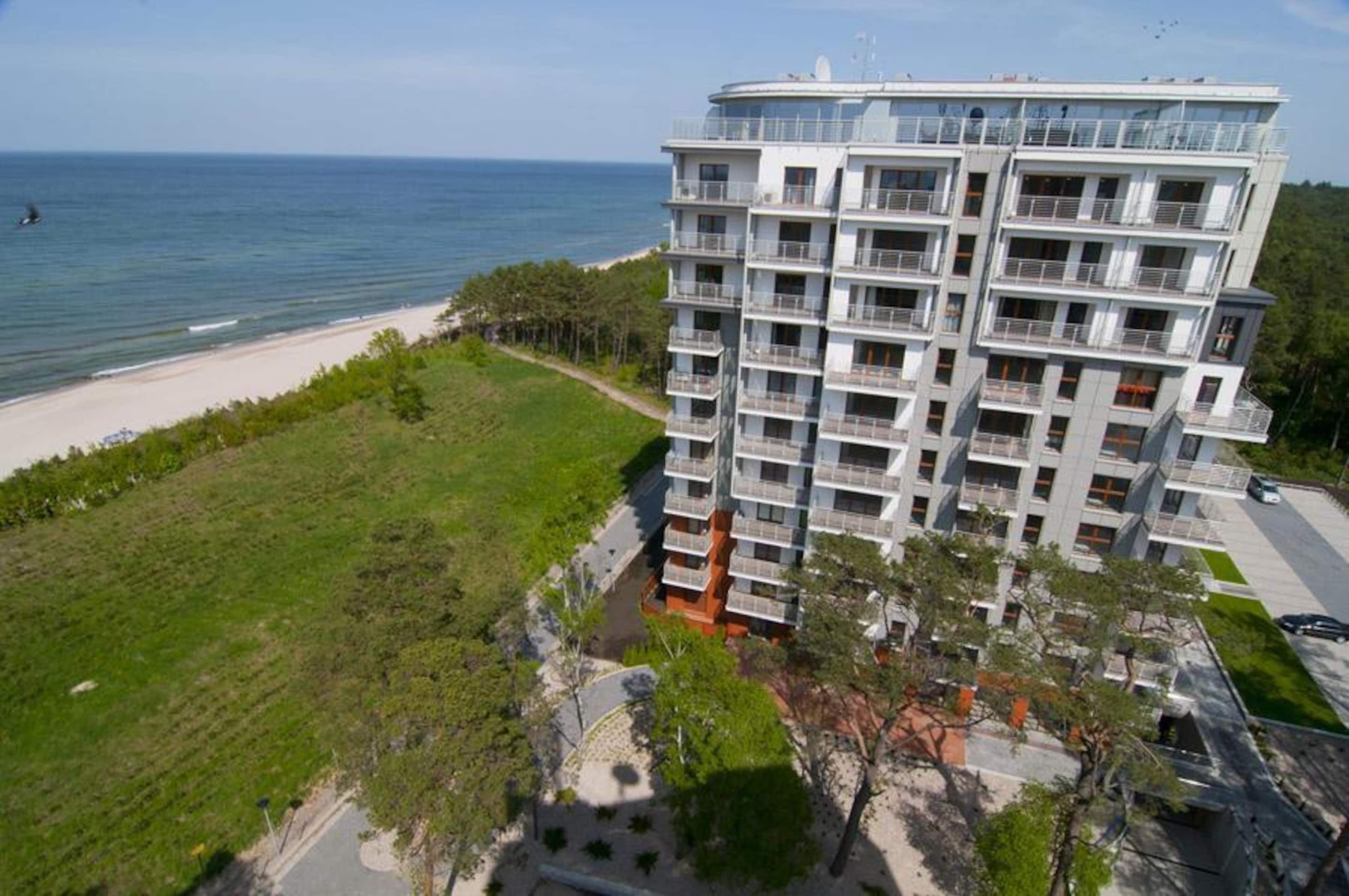 A multi-story hotel with balconies, located near a beach with a clear view of the ocean.