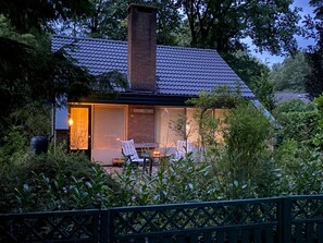 Uma casa moderna com telhado de telhas, chaminé de tijolos e porta de vidro que dá para um alpendre com mesa e cadeiras.