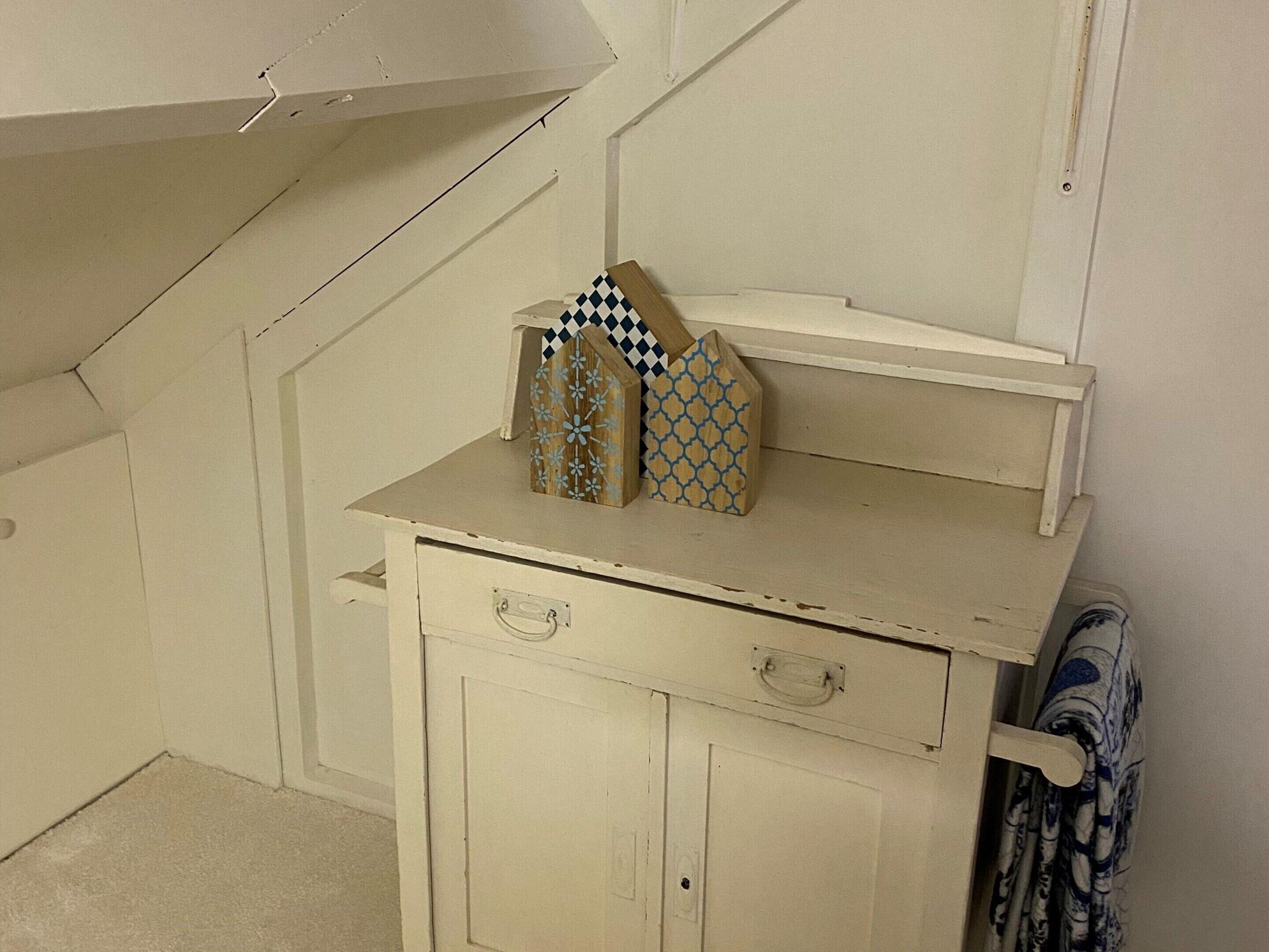 A white cabinet with two decorative wooden houses on top, a drawer with a handle, and a towel rack with a patterned towel.