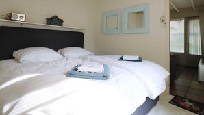 A bedroom with a bed, white bedding, a radio, and two wall-mounted mirrors.