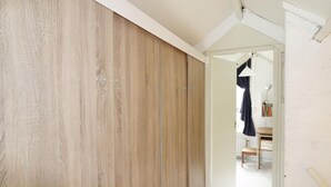 A hallway with a wooden wardrobe and a mirror reflecting a room with a chair and a table.