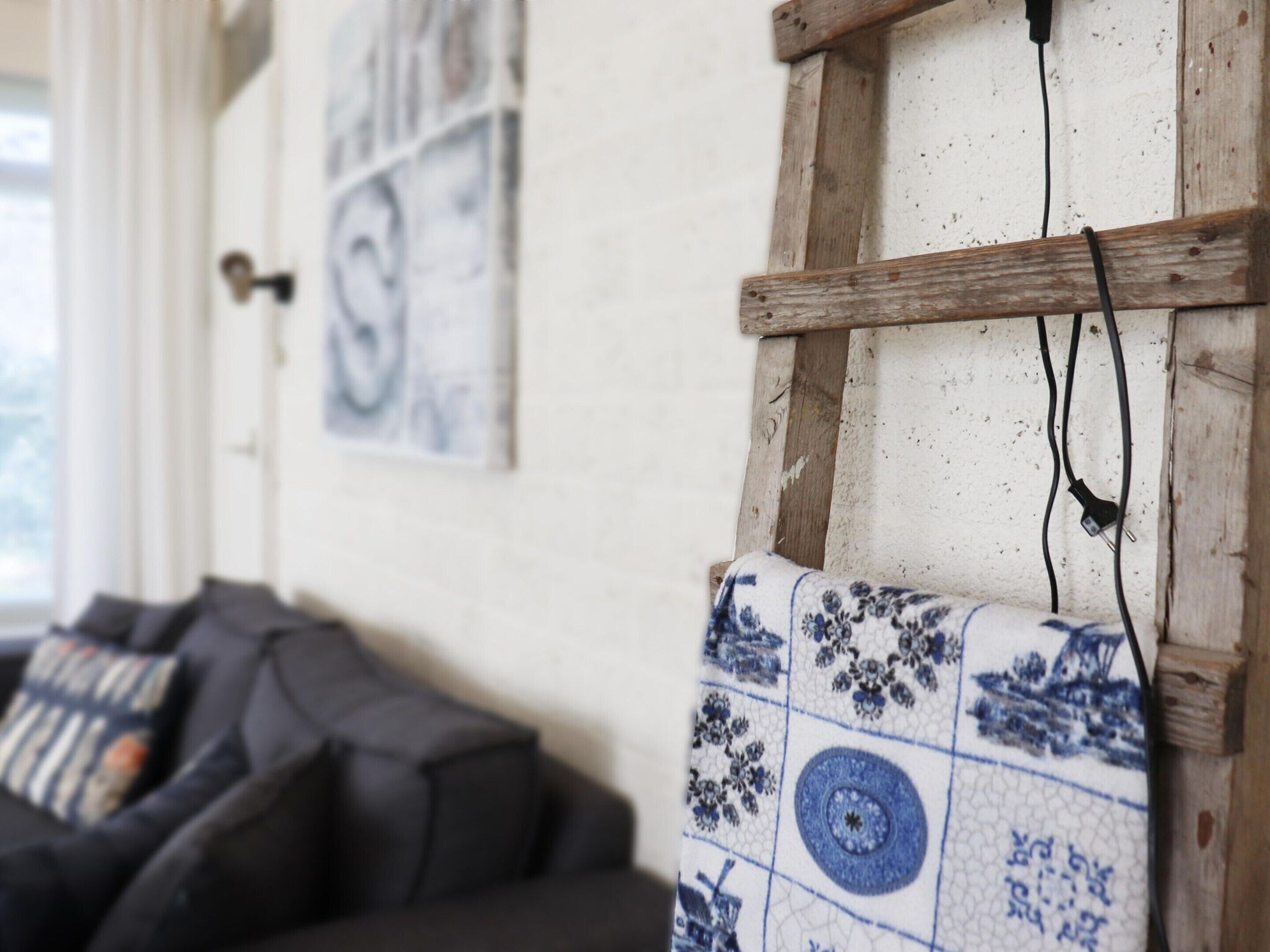 Une pièce avec une échelle en bois, une prise électrique fixée au mur et un coussin à motifs.
