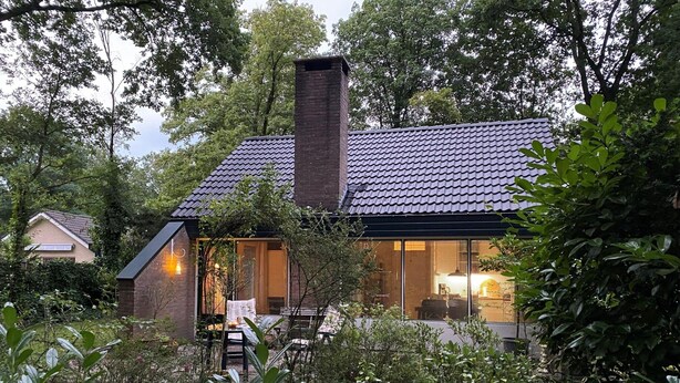 A cozy house with a tiled roof, large windows, and a brick chimney.