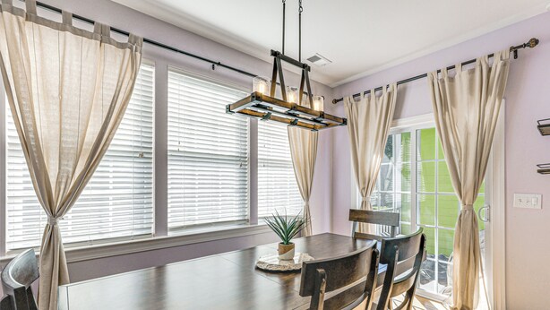 A dining area with a wooden table, chairs, a hanging light fixture, and a view through the window. - Townhome 3 Mi to Wescott Park & Golf Course! (Ladson)