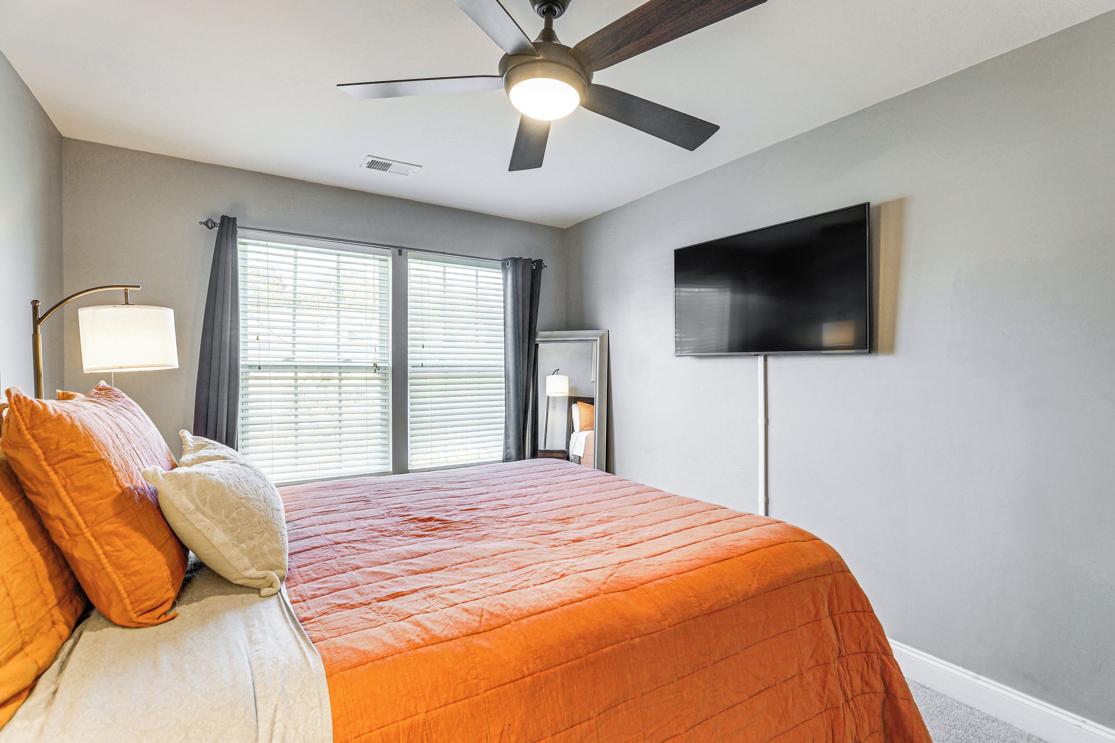 Ein Schlafzimmer mit Bett, Deckenventilator, Fernseher und Fenster mit Jalousien.