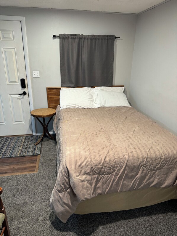 A bedroom with a bed, a bedside table, a chair, a door, and a curtain.