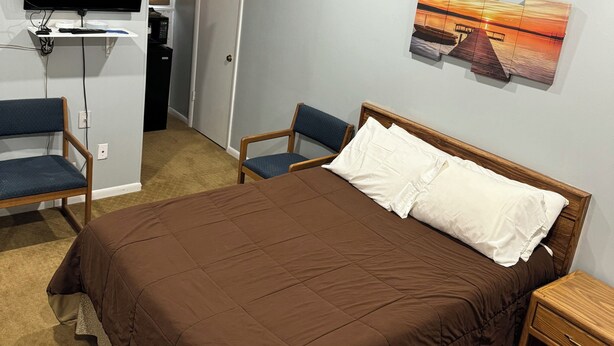 A hotel room with a bed, a TV, a desk, and a painting on the wall.